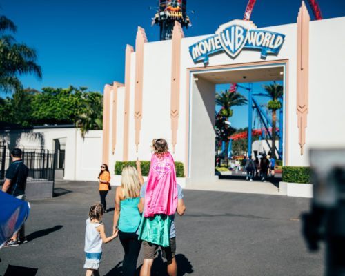 daughter-in-pink-supergirl-costume-on-fathers-shoulders-with-family-at-movie-world-entrance