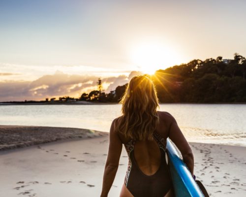 girl-walking-along-beach-with-paddleboard-at-sunrise-at-currumbin-creek