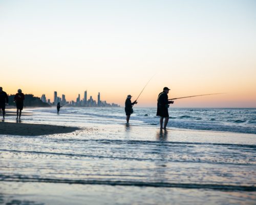 men-with-fishing-poles-on-the-beach-at-currumbin-burleigh-with-surfers-paradise-skyline